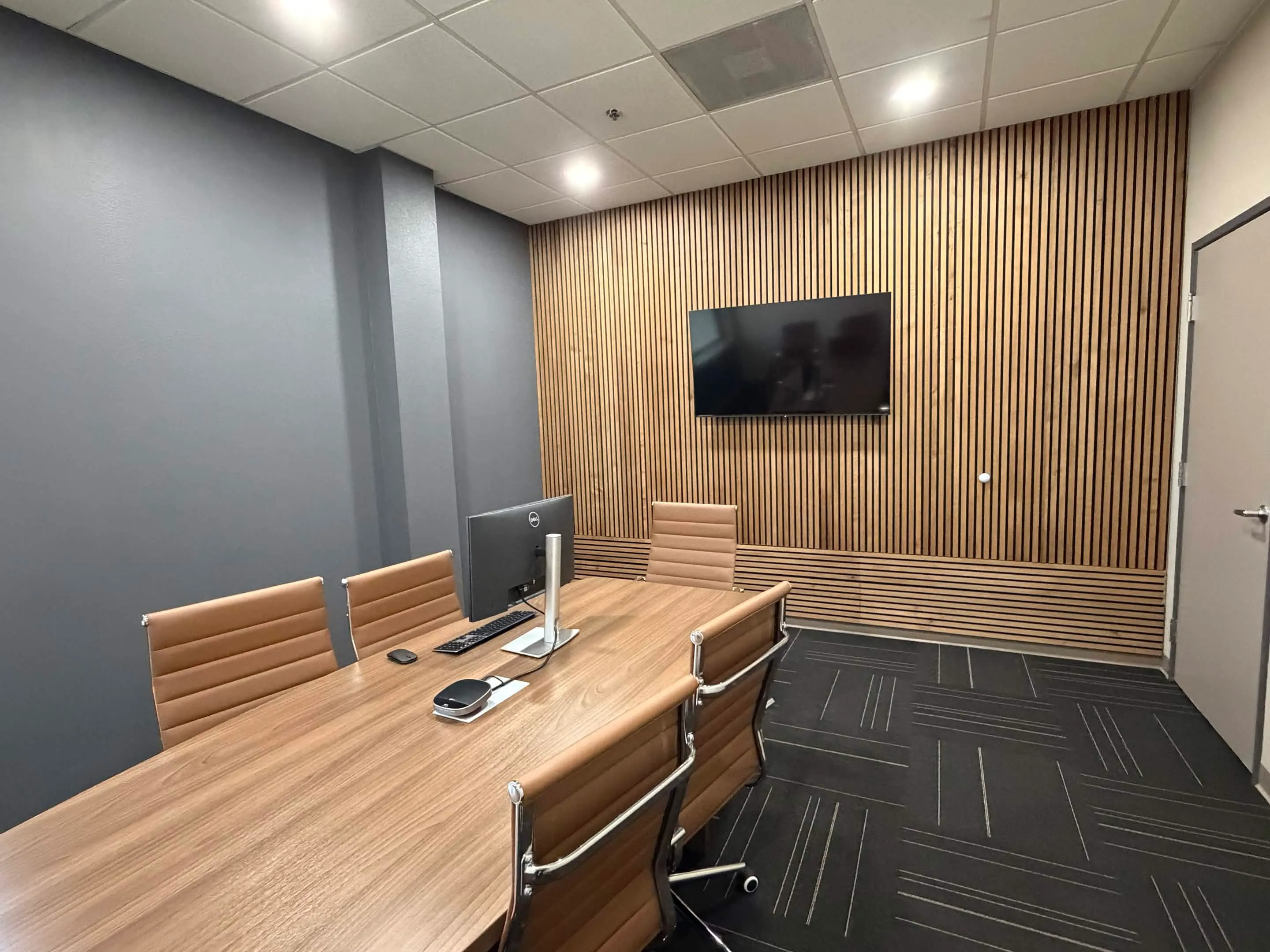 Conference room with a wood table, leather chairs, and a wall-mounted screen